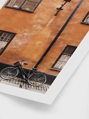 Schwarzes Fahrrad vor orangefarbener Hauswand mit Fenstern und Kopfsteinpflaster