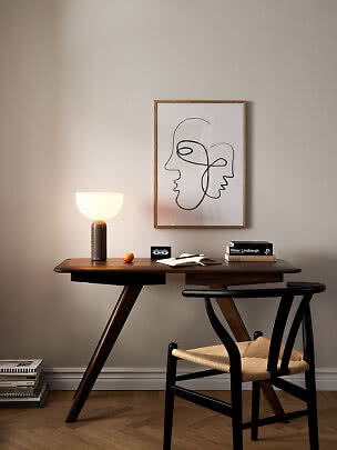 Dark wooden desk with chair, glowing table lamp, and framed abstract face line art on the wall