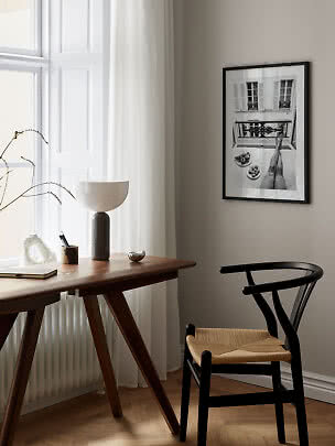 Angolo minimalista con scrivania in legno, sedia nera, lampada da tavolo e foto in bianco e nero incorniciata.