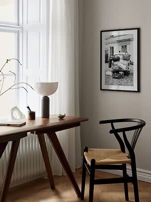 Minimalistisk hjemmekontor med træbord, sort stol og indrammet sort-hvid plakat på væggen