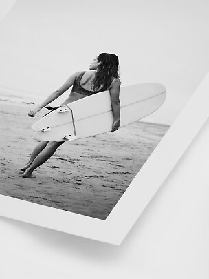 Sort-hvidt foto af kvinde på stranden med surfbræt under armen