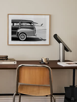 Home workspace with wooden chair, dark desk, modern table lamp and framed black-and-white car print