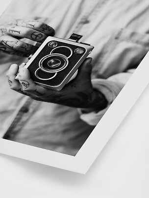 Foto in bianco e nero di mani tatuate che tengono una fotocamera vintage