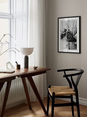 Angolo studio minimalista con scrivania in legno, sedia nera, lampada e foto in bianco e nero.