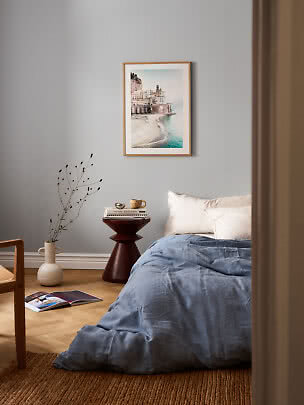 Bedroom with blue bedding, small side table, and framed coastal print on a gray wall