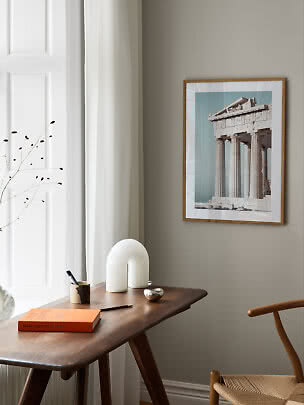 Framed print of a classical temple above a wooden desk by a window