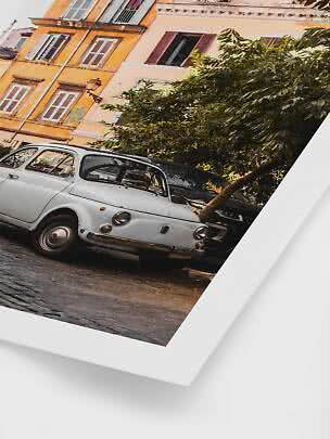 Classic white car parked on a cobblestone street by colorful buildings and trees