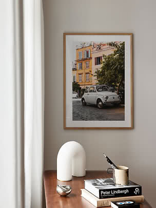 Framed photo print of a white vintage car by colorful buildings above a wooden table with books and decor