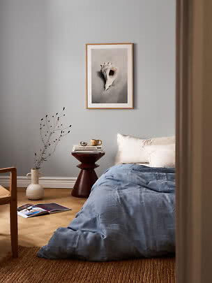 Chambre avec linge de lit bleu et affiche coquillage encadrée sur mur gris