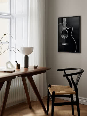 Black framed guitar wall art above a wooden desk with lamp and black chair