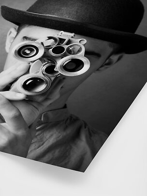 Black-and-white photo of a person in a black hat holding an optical device to their face