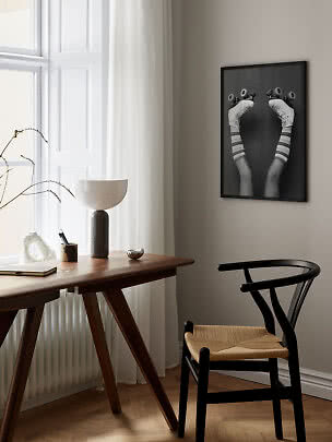 Schwarz gerahmtes Poster mit Beinen auf Rollschuhen über einem Holztisch im hellen Raum