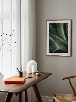 Affiche botanique encadrée au-dessus d'une table en bois avec livre, vase et chaise, pièce lumineuse