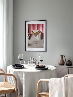 Eethoek met ronde tafel, zwarte borden, wijnglazen en ingelijste cocktailposter aan grijze muur
