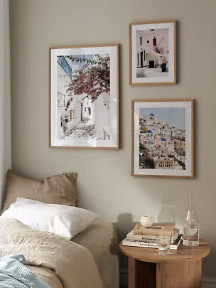 Bedroom with three framed travel prints above the bed and a round wooden bedside table