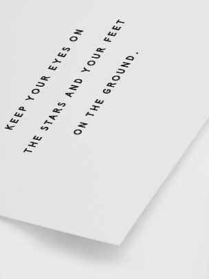 Hvid plakat med sort tekst: “Keep your eyes on the stars and your feet on the ground.”