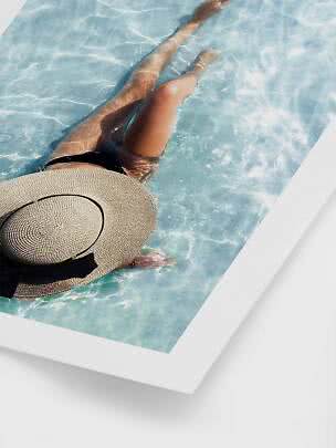 Person in a black swimsuit and large straw hat floating in a light blue pool