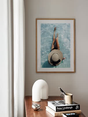 Framed photo of a person in light blue pool water above a wooden table with books and decor