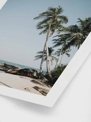 Indrammet foto af palmer på sandstrand med klipper og hav under blå himmel