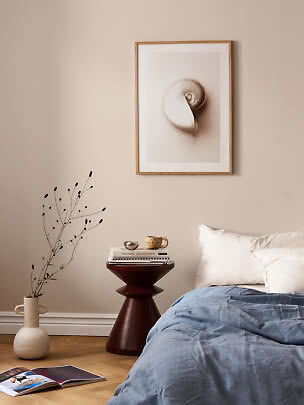 Shell print in a light wood frame above a bed and side table in a calm bedroom