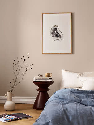 Bedroom with framed oyster artwork above bed, blue duvet, side table and floor vase