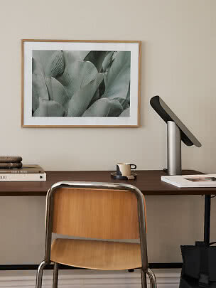 Homeoffice mit Holzstuhl, Schreibtischlampe und gerahmtem Blätterbild an der Wand