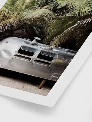 Silver trailer on sand beneath palm leaves, shown as a framed print