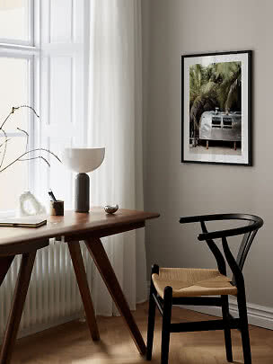 Black framed print of a silver trailer among palm trees above a wooden desk and chair
