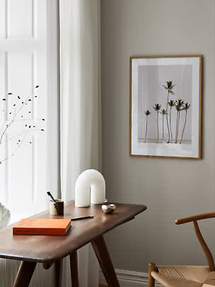 Framed palm tree print on wall above a wooden desk by a bright window