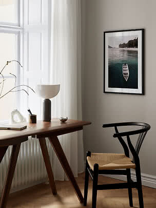 Framed photo of a boat on calm water hanging above a desk in a bright room.