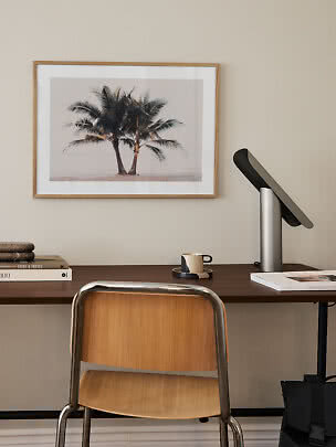 Escritorio con silla de madera, lámpara negra y cuadro de palmeras en pared beige