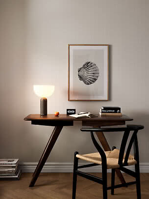 Dark wooden desk with lit table lamp, chair, and framed shell print on a beige wall