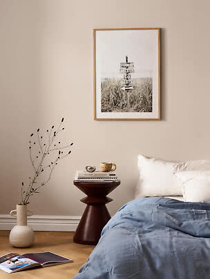 Schlafzimmer mit gerahmtem Strandposter über dem Bett, rundem Beistelltisch und Bodenvase
