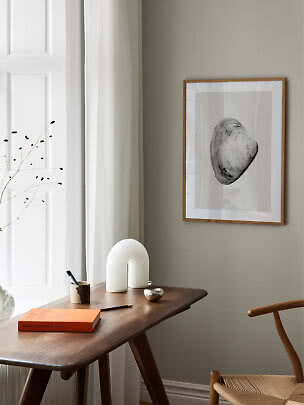 Art print in a light wood frame with black shell on a gray wall above a wooden desk