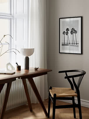 Espace bureau minimaliste avec bureau en bois, chaise noire, lampe de table et photo de palmiers