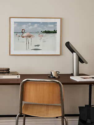 Ingelijste flamingoposter boven bureau met stoel, lamp, boeken en mok