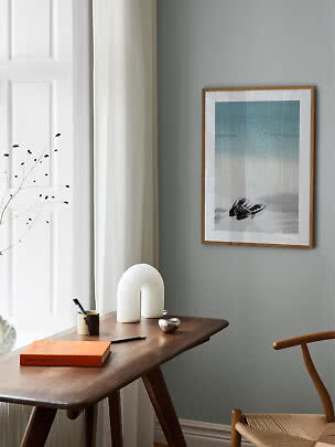 Donkerhouten bureau met witte lamp, boek en ingelijste strandfoto aan grijze muur