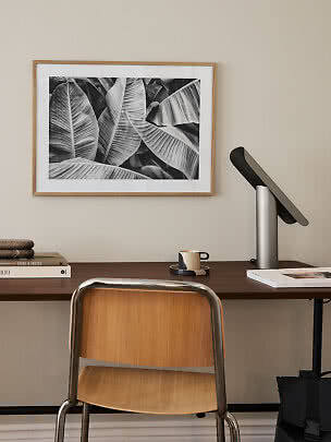 Bureau avec chaise et lampe sous une affiche encadrée de feuilles en noir et blanc
