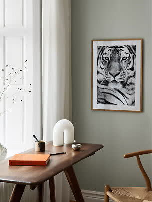 Inramad svartvit tigerbild på grå vägg ovanför ett träskrivbord vid ett fönster