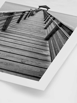 Black-and-white photo of a wooden pier with railings leading to a small shelter over the water