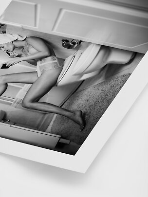 Schwarz-Weiß-Foto einer Frau im Spitzen-Body mit Handtuchturban, sitzend auf einer Toilette