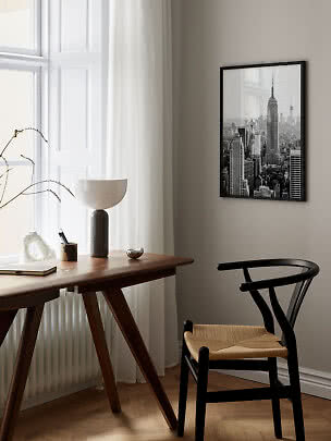 Sort indrammet plakat med New York-skyline over et skrivebord i et lyst, moderne rum