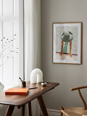 Dark wood desk with white table lamp, book, and framed wall art