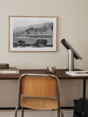 Scrivania con sedia in legno, lampada da tavolo e stampa Palm Springs incorniciata su parete beige