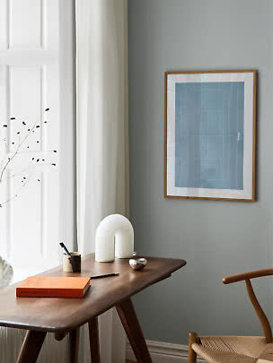 Bureau minimaliste avec table en bois, affiche bleue encadrée, lampe blanche et livre orange
