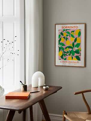 Affiche Sorrento encadrée avec citrons et feuilles vertes sur fond rose au-dessus d'un bureau en bois