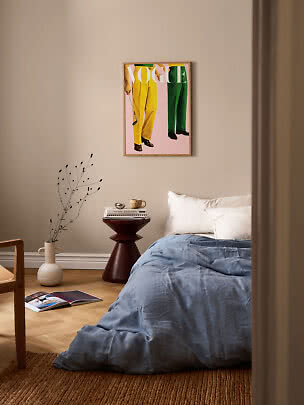 Bedroom with blue bedding, dark side table, vase, and framed Vogue poster on a beige wall