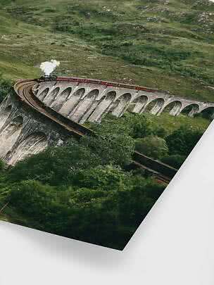 Steam train crossing a curved stone viaduct in a green hillside landscape