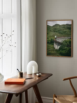 Framed poster of a steam train on a stone viaduct in green hills above a wooden desk