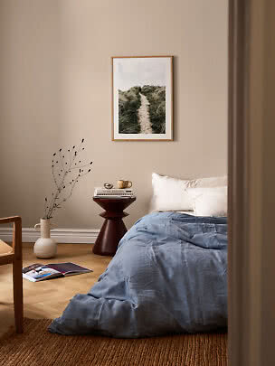 Camera da letto tranquilla con biancheria blu, cuscini bianchi, tavolino, vaso e stampa natura incorniciata